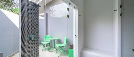 Une salle de bain moderne avec une cloison en verre, un espace douche et un coin salon avec des chaises vertes.