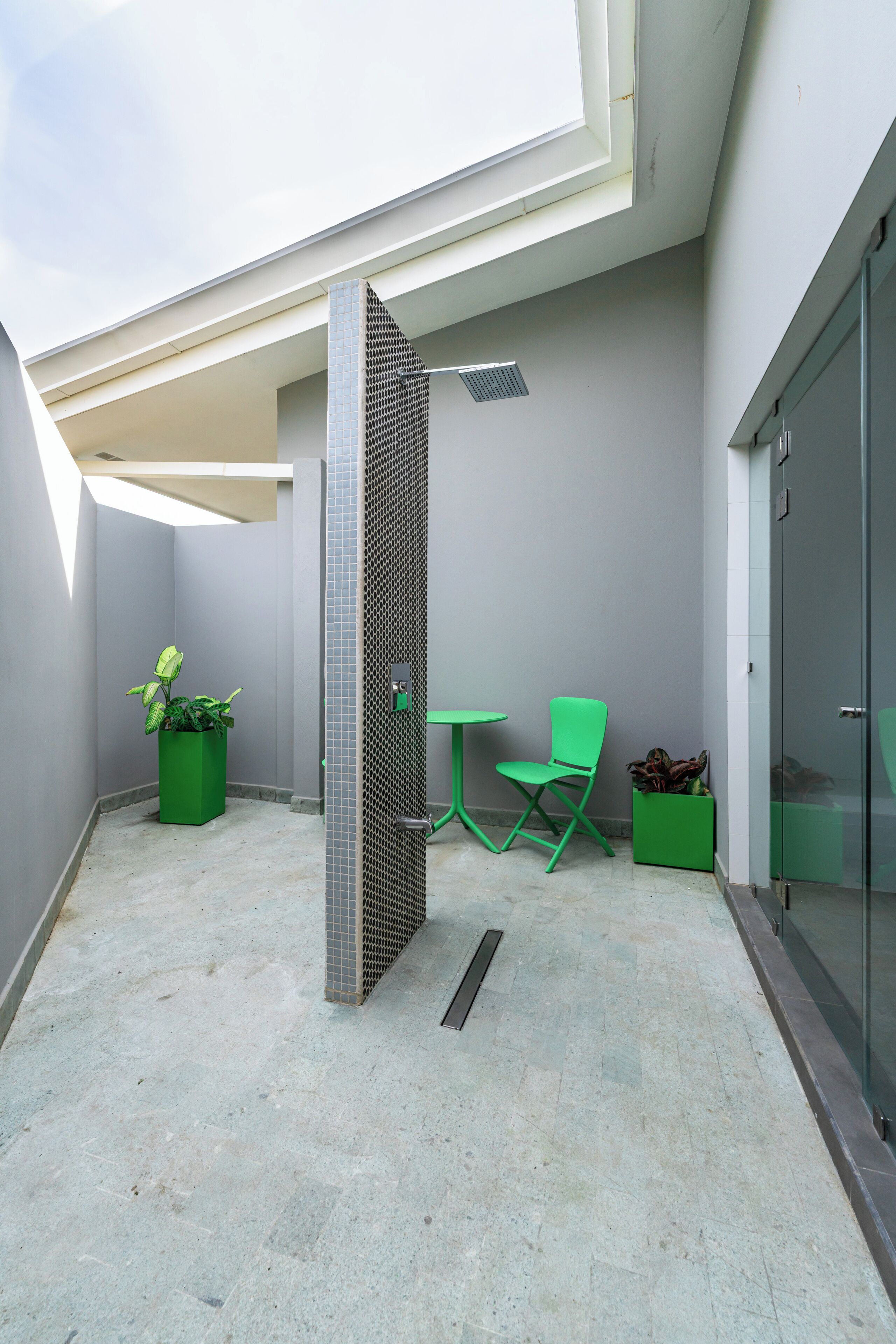 Ett modernt utomhusområde med en glasdörr, ett litet bord, en stol och krukväxter.