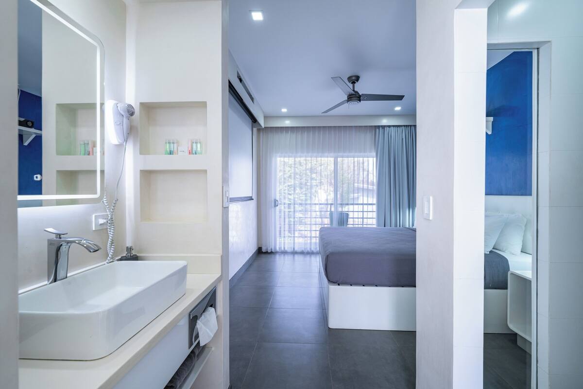 A modern hotel room with a large bathroom, a bed, and a ceiling fan.