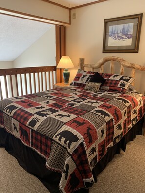 A bedroom with a large bed, a wooden headboard, a nightstand with a lamp, and a framed picture on the wall.