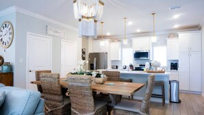 Una cocina moderna con armarios blancos, una isla central y un comedor con sillas de mimbre.