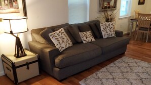 Una sala de estar con un sofá gris, una mesita auxiliar con una lámpara, piso de madera y una alfombra estampada.
