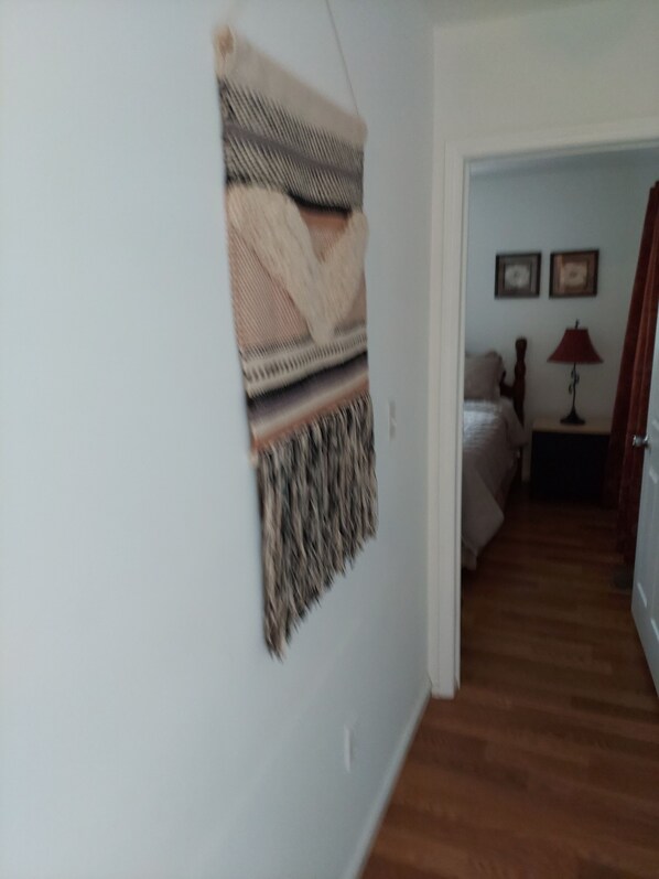 A hallway with a bed, a lamp, and a wall-mounted tapestry.