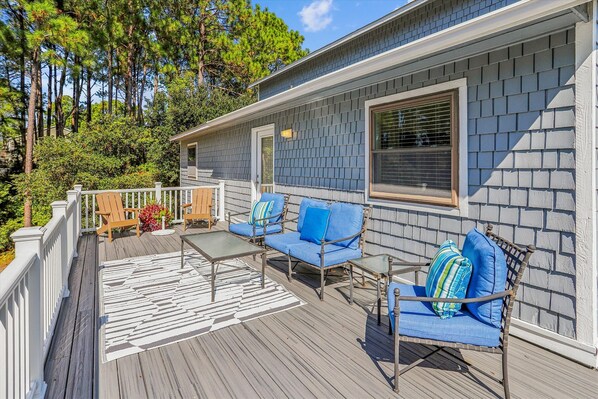 A covered deck with outdoor furniture, a railing, and a view of a house with a shingled exterior.