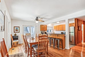 A spacious kitchen with wooden cabinets, a stainless steel refrigerator, and a dining area with wooden chairs and a table. - Private Heated Saltwater Pool, 5 min to beach, Screened porch (Corolla)
