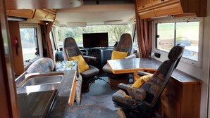 A compact RV interior with a kitchenette, a dining area, and a TV. - Large Static Motorhome-Stunning Countryside Views (Cirencester)