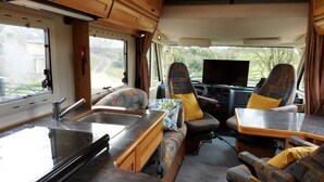 A compact RV interior with a kitchenette, seating area, and a TV. - Large Static Motorhome-Stunning Countryside Views (Cirencester)