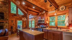 Una cocina de estilo rústico tipo cabaña, con una isla grande, armarios de madera y una chimenea de piedra.