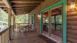 Eine Holzterrasse mit Tisch und Stühlen, Holzgeländern und Blick auf den Wald.