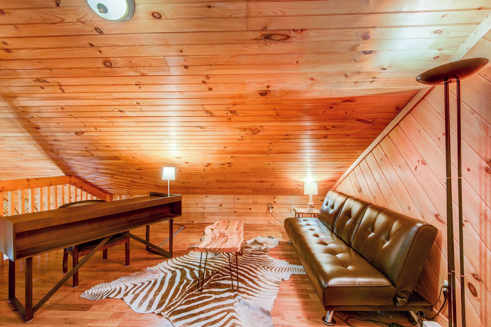 A cozy cabin interior with a wooden ceiling, a leather couch, a wooden bench, and a zebra-patterned rug.