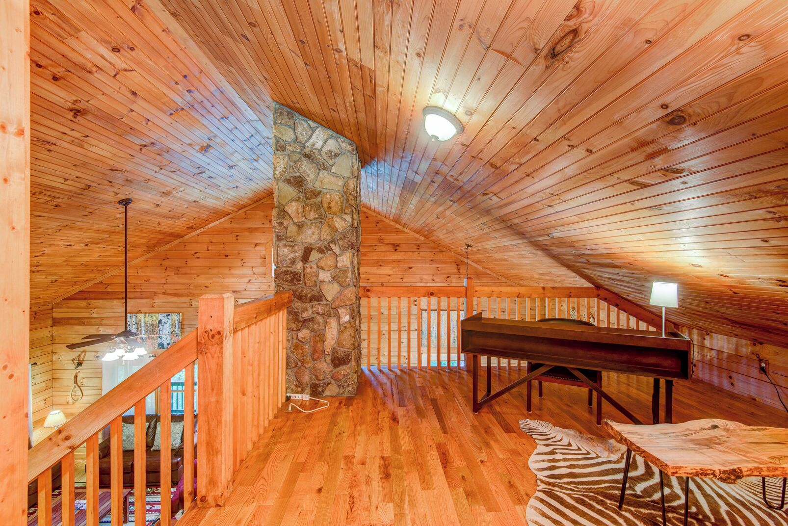 A wooden interior with a stone pillar, a piano, and a zebra-patterned rug.