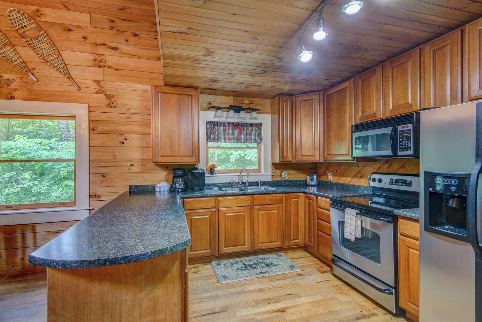 A kitchen with wooden cabinets, granite countertops, a stainless steel refrigerator, and a microwave.