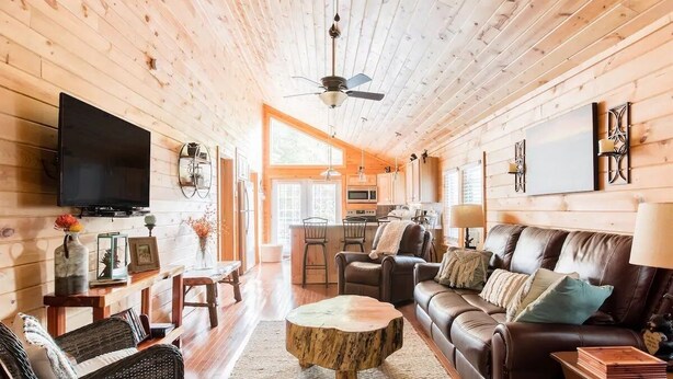 A cozy cabin interior with a wooden interior, a flat-screen TV, a dining area, a sofa, and a ceiling fan. - Cozy, romantic cabin in beautiful Roan Mt Tennessee & hot tub (Roan Mountain)