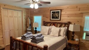 A wooden room with a bed, two bedside tables, a ceiling fan, and a framed picture on the wall. - Cozy, romantic cabin in beautiful Roan Mt Tennessee & hot tub (Roan Mountain)