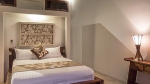 Una cama bien hecha con una colcha estampada con motivos florales, una escultura de Buda montada en la pared y una mesita de noche con una lámpara.