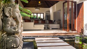 Un interior moderno con un sofá blanco, una escultura decorativa de un elefante y una terraza de madera que da a una piscina.