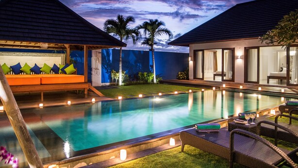 Una piscina con sillas de descanso y velas, rodeada por un césped cuidado y palmeras.