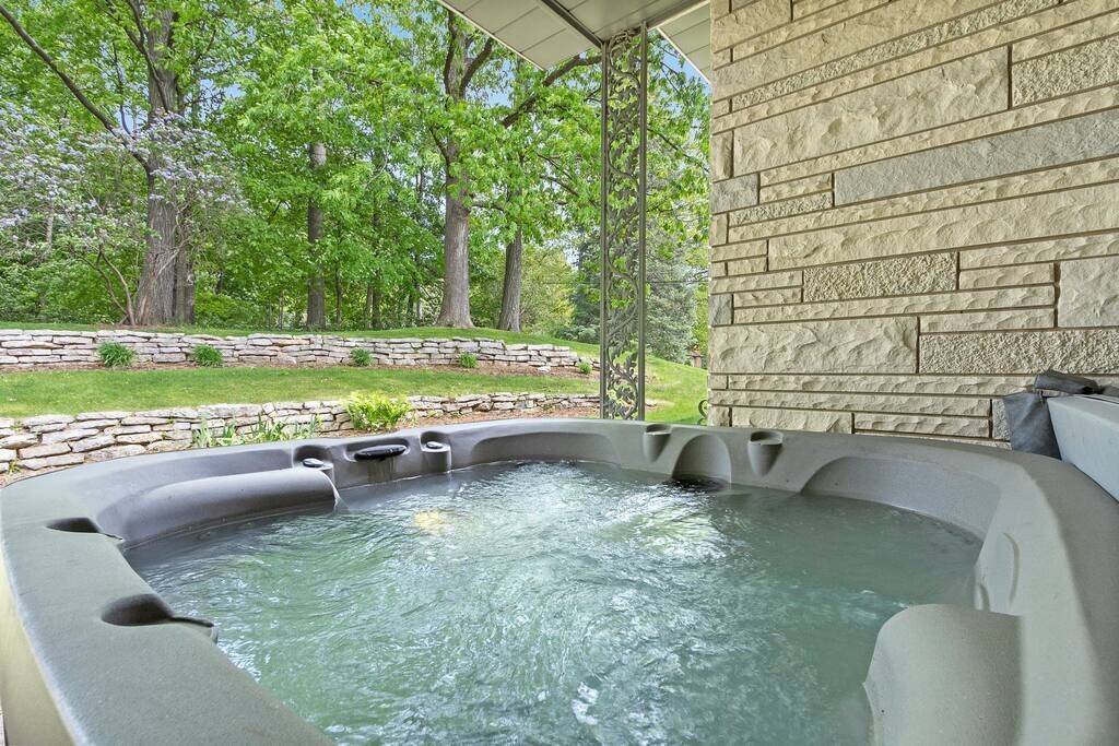 A hot tub with a stone wall backdrop, surrounded by a stone retaining wall and greenery.