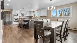 Una cocina moderna con una isla central, armarios blancos y un comedor con una mesa grande y sillas.