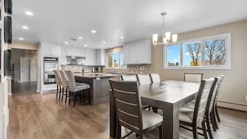 A modern kitchen with a central island, white cabinetry, and a dining area with a large table and chairs.