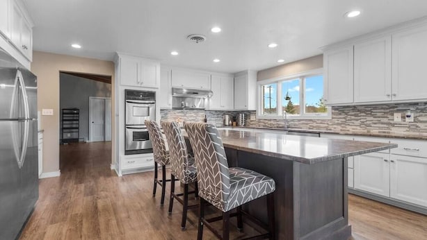 Una cocina moderna con armarios blancos, una isla grande con taburetes y vistas al exterior.