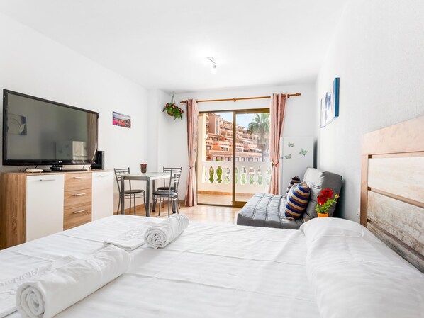 Ein Hotelzimmer mit Bett, Fernseher, Schreibtisch und einem Balkon mit Blick auf Gebäude.