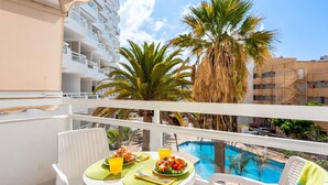 Ein Balkon mit Esstisch für zwei Personen, Blick auf Pool und Palmen.