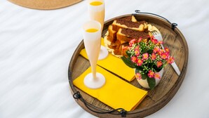 Ein Holztablett mit einem Getränk, einer kleinen Pflanze und einem Kuchenstück auf einer weißen Tischdecke.