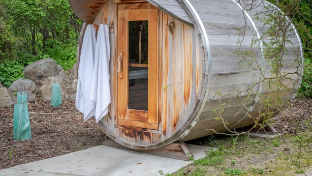 A cylindrical wooden structure with a door, a towel hanging on the door, and a small step leading up to it.