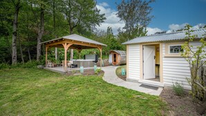 A rustic cabin with a covered outdoor seating area, a hot tub, and a small shed.