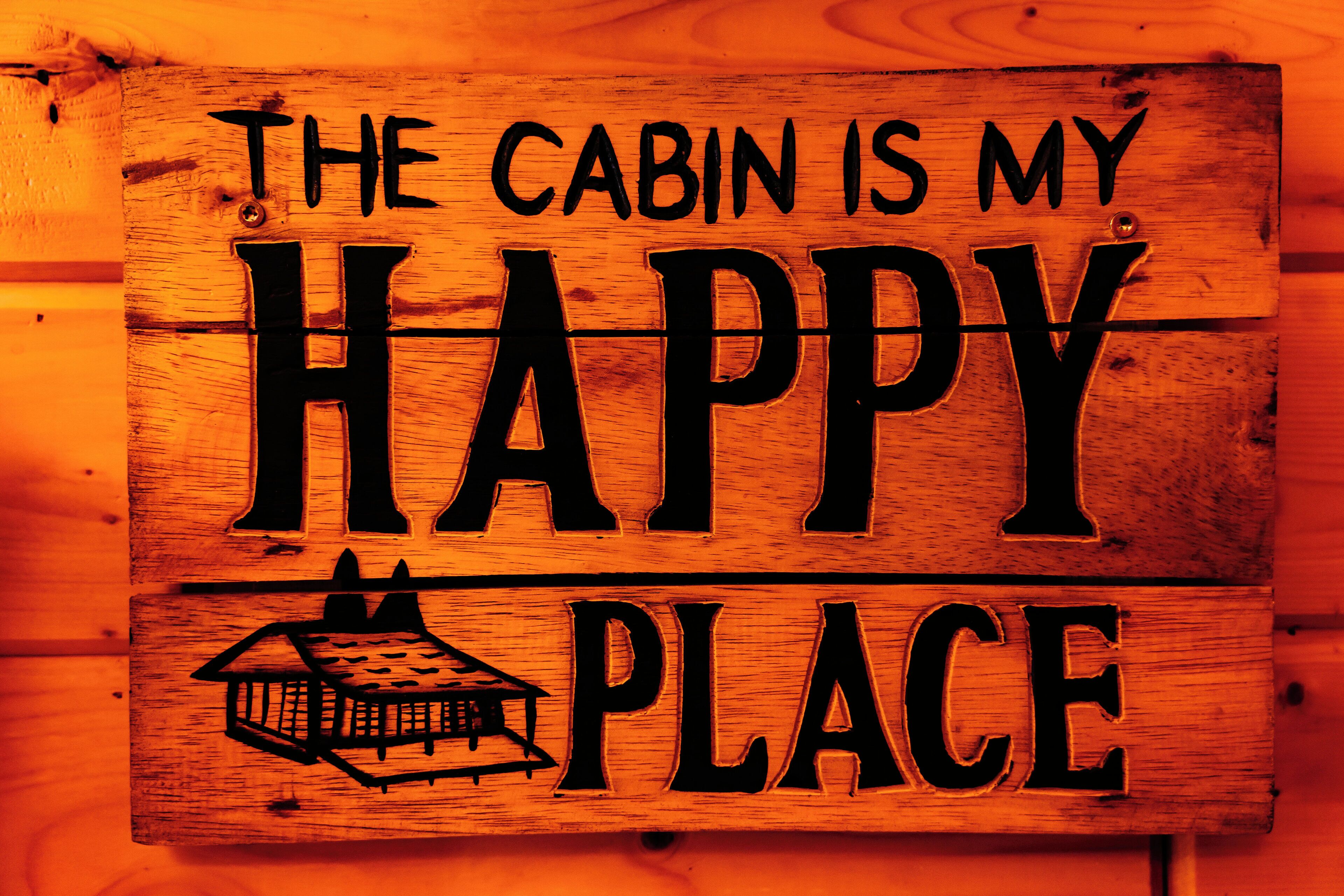 A wooden sign with the text "THE CABIN IS MY HAPPY PLACE" and a small cabin illustration.