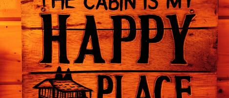 A wooden sign with the text "THE CABIN IS MY HAPPY PLACE" and a small cabin illustration.