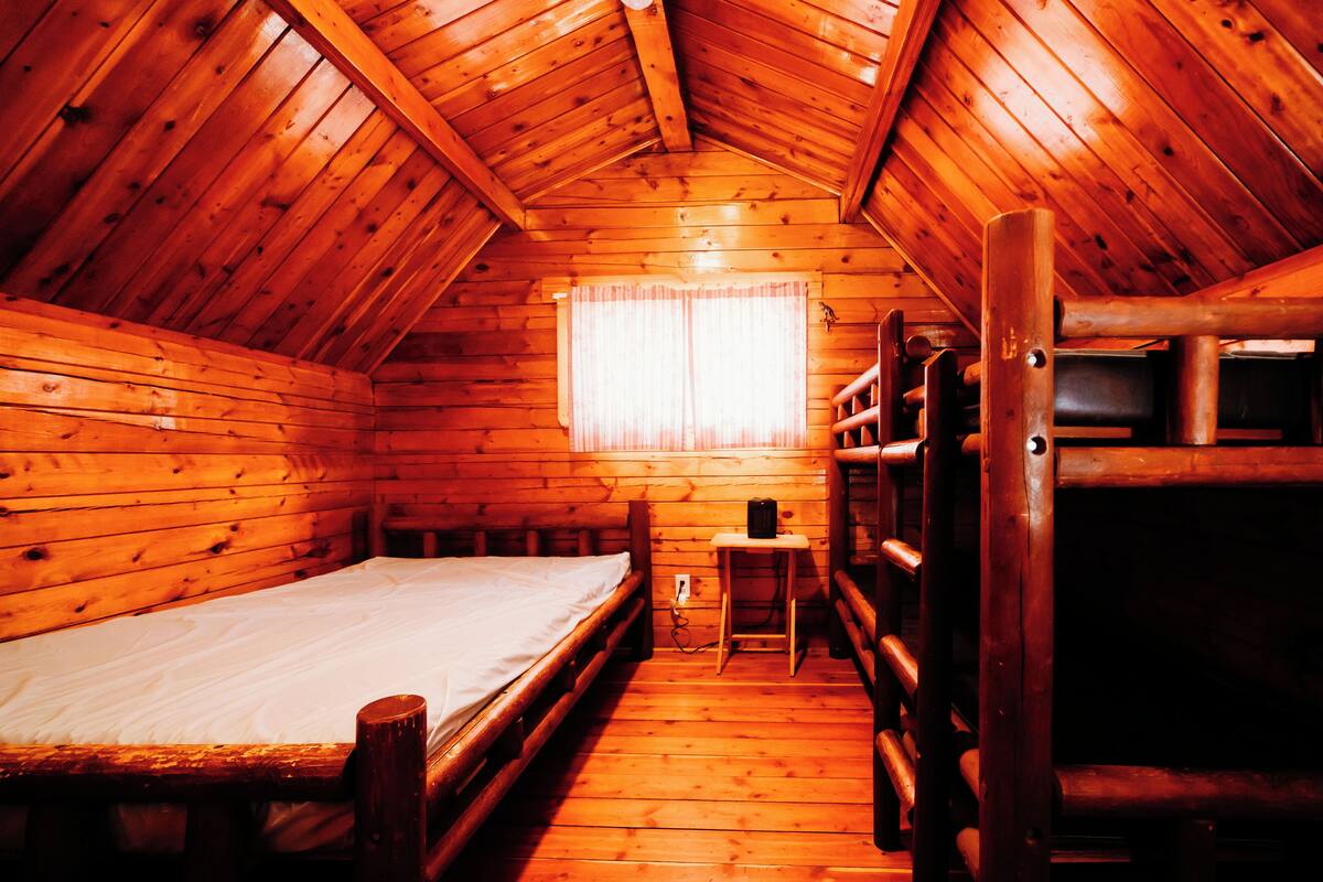 A wooden cabin with a bunk bed, a small table, and a window with curtains.