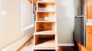A wooden staircase leading to a lofted area with a modern kitchen and a built-in shelving unit. - La Junta Camping & Cabins (La Junta)