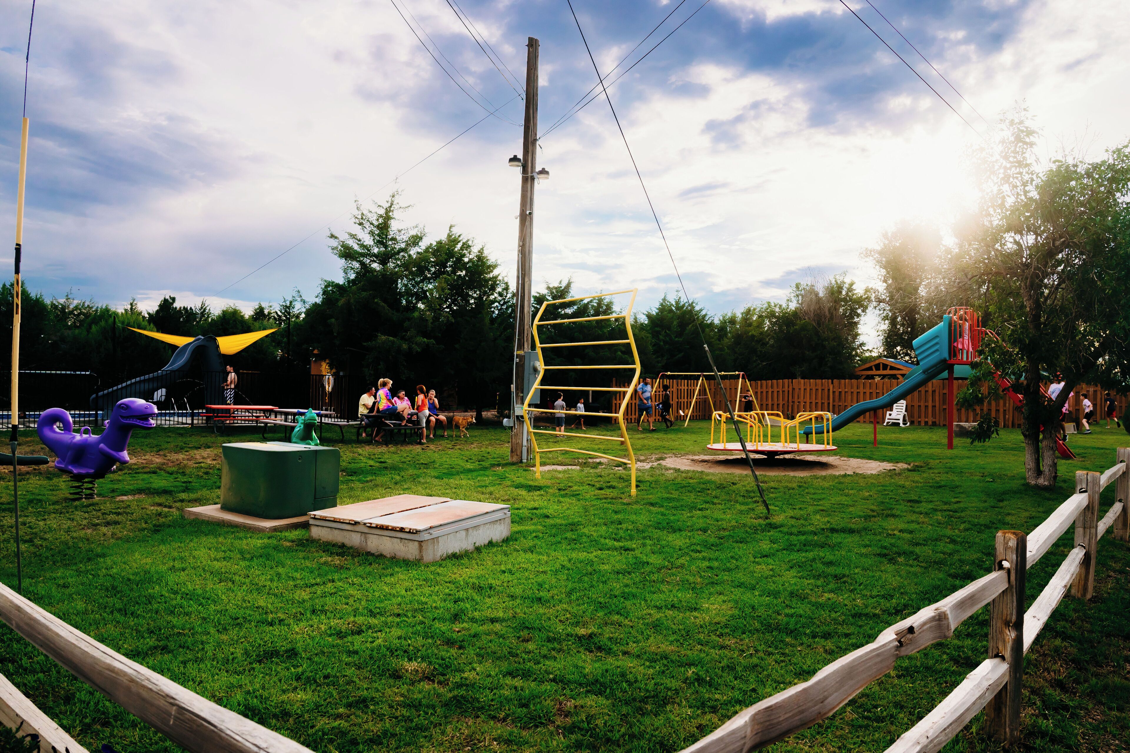A playground with various play structures, a wooden fence, and a grassy area.