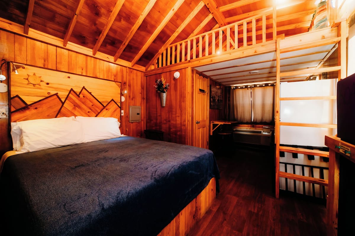 A wooden cabin interior with a bunk bed, a small kitchenette, and a wooden ceiling.