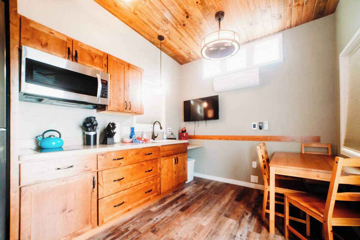 A kitchen with wooden cabinets, a microwave, a sink, and a dining area with chairs.
