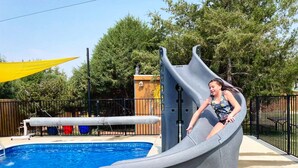 A water slide adjacent to a swimming pool with a wooden deck and a fenced area. - La Junta Camping & Cabins (La Junta)