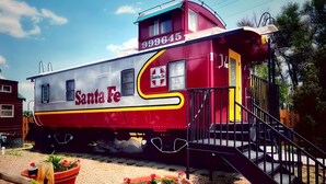 A stationary train car with 'Santa Fe' branding, a yellow and red color scheme, and a small porch with steps. - La Junta Camping & Cabins (La Junta)