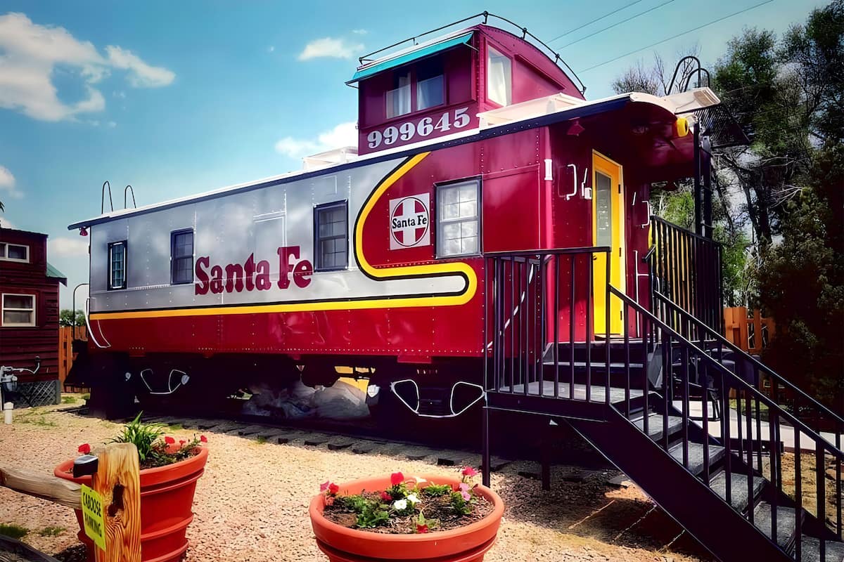 A stationary train car with 'Santa Fe' branding, a yellow and red color scheme, and a small porch with steps.