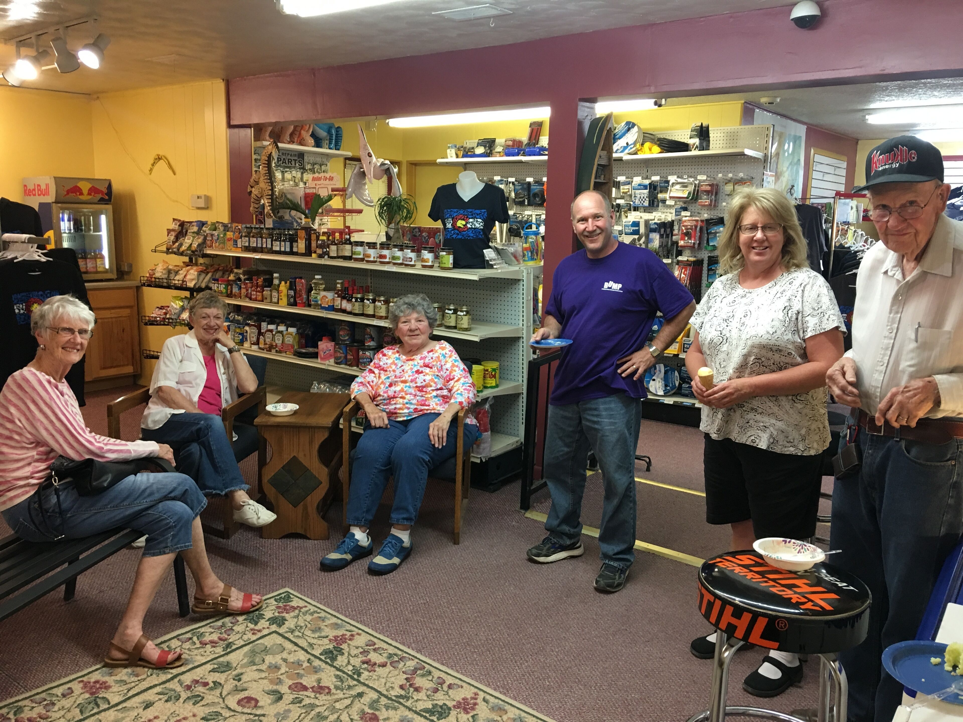 A group of people in a store with shelves stocked with various items, a wheelchair, and a stool with a hockey puck.