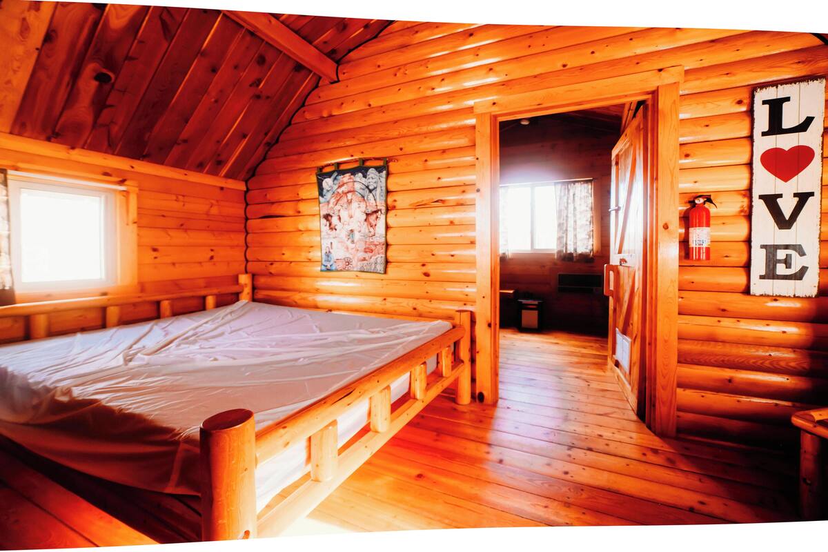 A wooden cabin room with a bed, a 'LOVE' sign, and a wooden door.