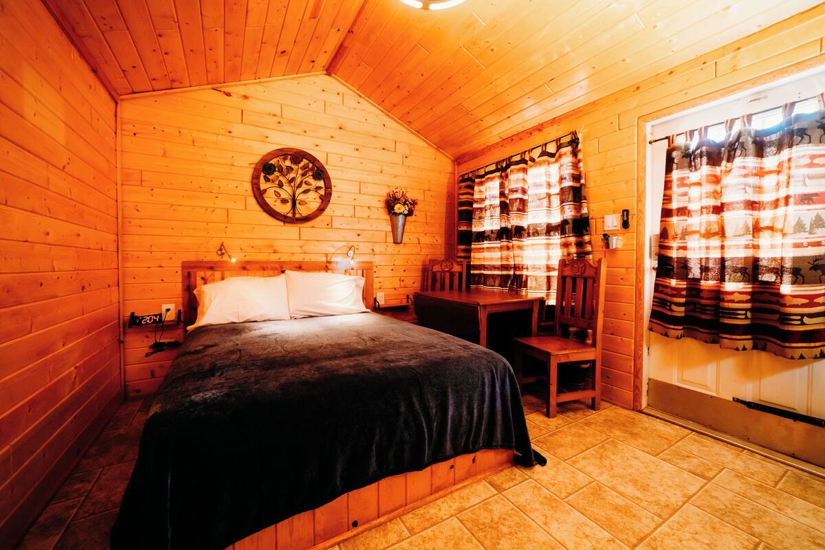 A cozy wooden cabin room with a bed, a small table, and a chair.