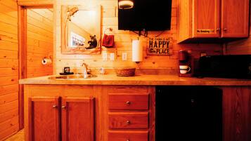 Cocina de cabaña de madera con encimera de madera, un fregadero, una estufa, un microondas y un televisor montado sobre la encimera.