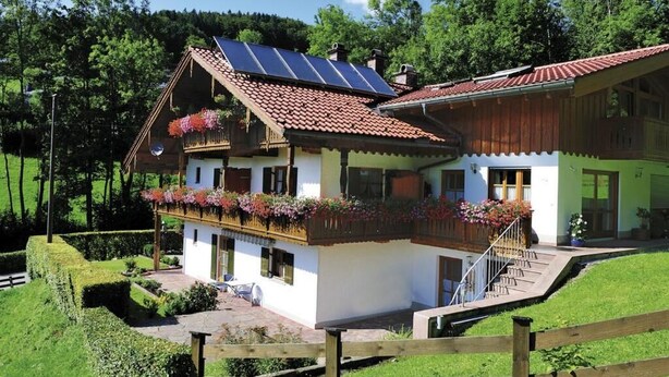 Een chalet met twee verdiepingen, een schuin dak, zonnepanelen en een balkon met bloembakken.