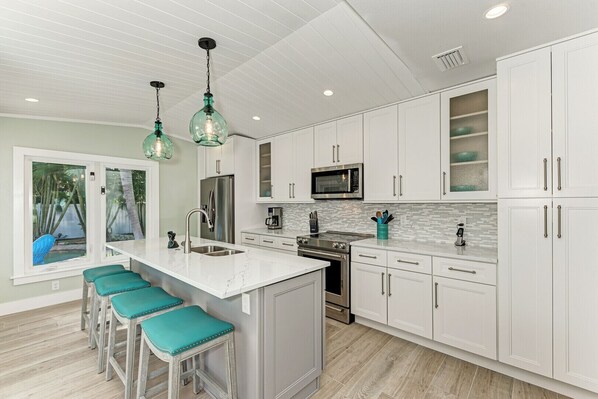 Una cocina moderna con armarios blancos, electrodomésticos de acero inoxidable, una isla grande con taburetes de bar e iluminación colgante.