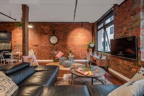 A modern living room with a brick wall, leather sofa, round coffee table, and a flat-screen TV.