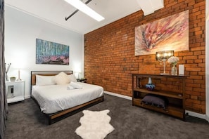 Relax in a serene bedroom with a large bed, a brick accent wall, and a painting above.