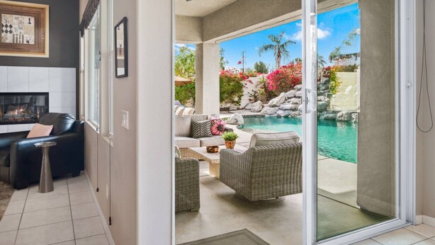 Un salon moderne doté d’une cheminée, d’un coin repas et d’une porte-fenêtre coulissante donnant sur une terrasse extérieure avec une piscine et un aménagement paysager de style tropical.