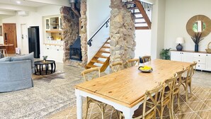 A spacious living area with a wooden dining table, a grey sofa, and a stone fireplace.